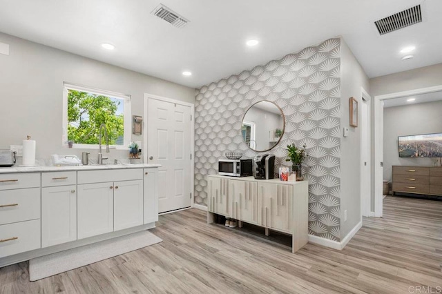 bar with white cabinets, light hardwood / wood-style flooring, and sink