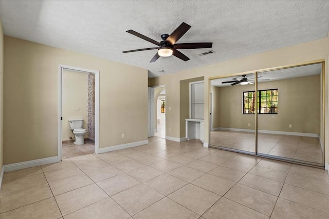 unfurnished bedroom featuring ensuite bathroom, a textured ceiling, ceiling fan, light tile patterned floors, and a closet