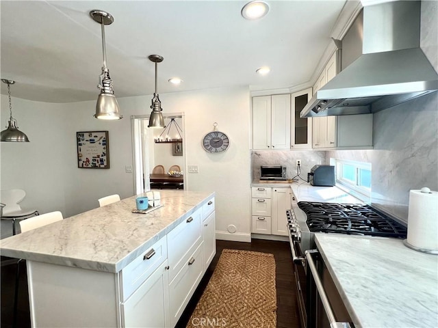 kitchen featuring stainless steel range, white cabinetry, decorative light fixtures, and wall chimney range hood