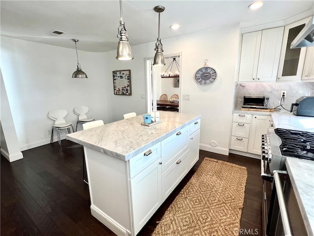 kitchen featuring decorative light fixtures, tasteful backsplash, a center island, white cabinetry, and light stone counters