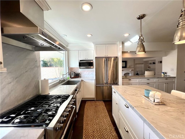 kitchen with decorative light fixtures, wall chimney range hood, sink, high end appliances, and white cabinets