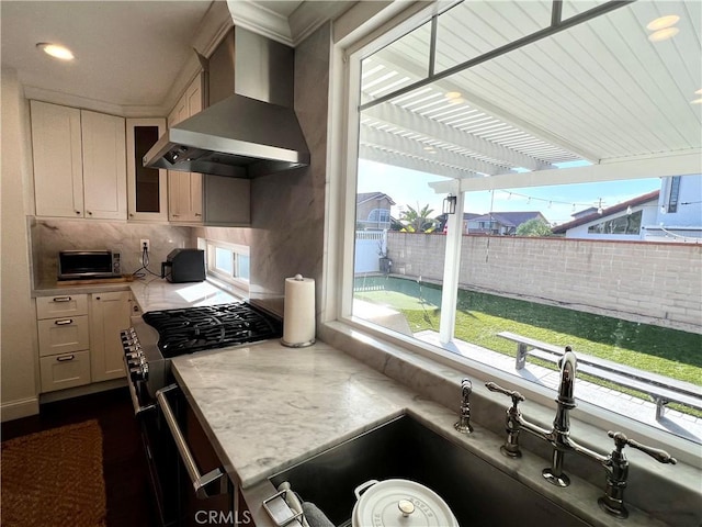 kitchen with white cabinets, a healthy amount of sunlight, sink, and wall chimney range hood