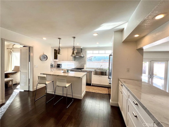 kitchen featuring light stone countertops, white cabinetry, pendant lighting, and wall chimney range hood