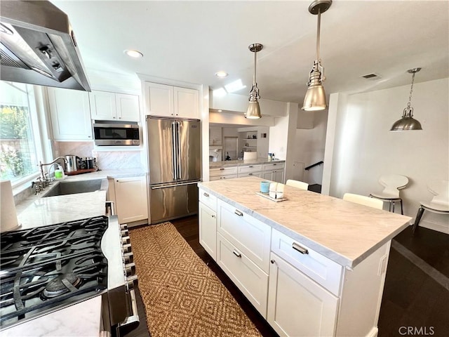 kitchen featuring pendant lighting, appliances with stainless steel finishes, a center island, extractor fan, and white cabinetry