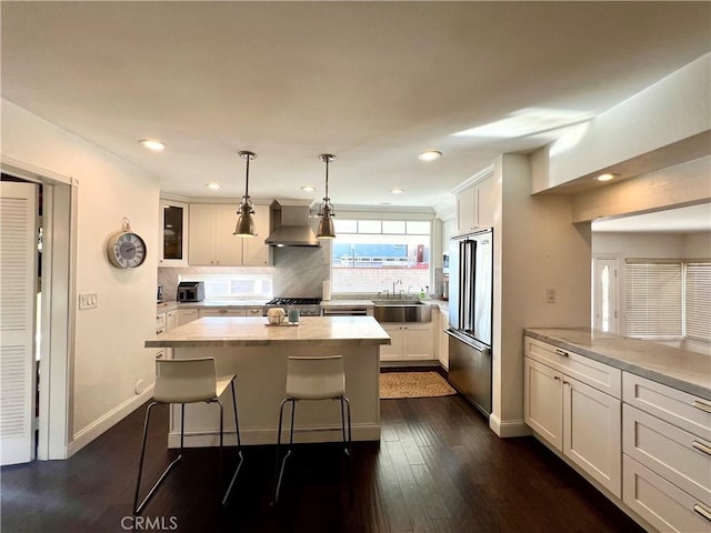 kitchen featuring pendant lighting, wall chimney range hood, stainless steel appliances, decorative backsplash, and sink