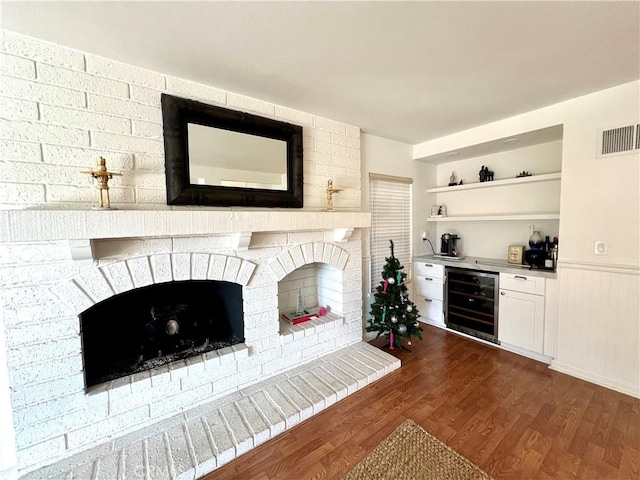 unfurnished living room featuring dark wood-type flooring, a brick fireplace, wine cooler, and bar area