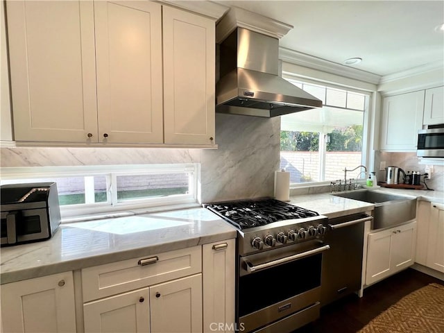 kitchen with white cabinetry, stainless steel appliances, tasteful backsplash, light stone countertops, and wall chimney exhaust hood