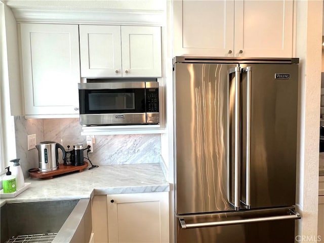 kitchen featuring white cabinets, backsplash, light stone counters, and stainless steel appliances