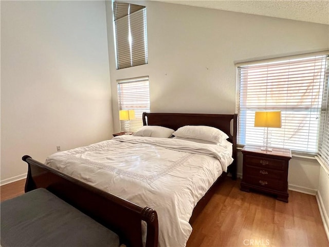 bedroom featuring wood-type flooring, a textured ceiling, and lofted ceiling