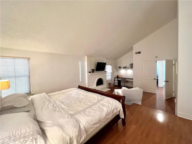 bedroom featuring high vaulted ceiling, a textured ceiling, dark hardwood / wood-style floors, and a fireplace