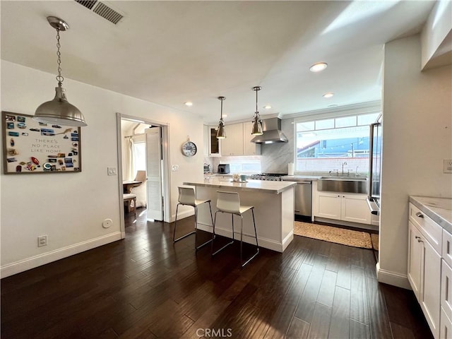 kitchen featuring hanging light fixtures, white cabinets, wall chimney range hood, and a kitchen island