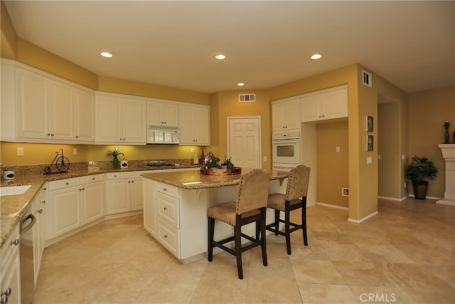 kitchen featuring white cabinets, a kitchen island, appliances with stainless steel finishes, a breakfast bar, and light stone counters