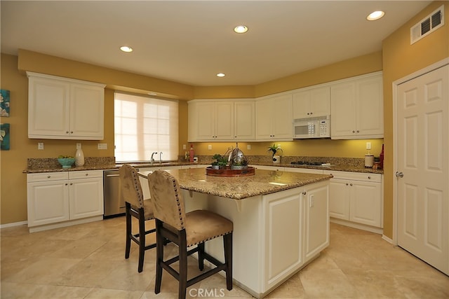 kitchen featuring stone counters, appliances with stainless steel finishes, a kitchen island, and white cabinets