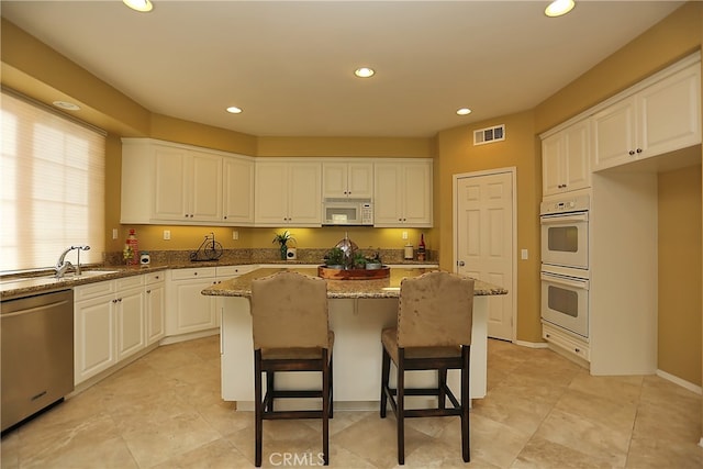 kitchen featuring white appliances, stone countertops, a center island, and white cabinets