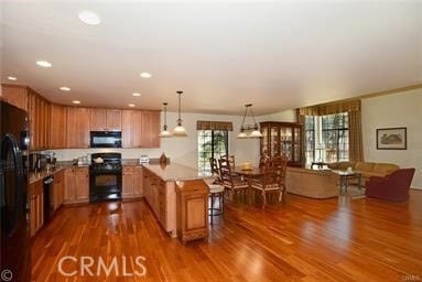 kitchen with black appliances, dark hardwood / wood-style flooring, kitchen peninsula, pendant lighting, and a breakfast bar