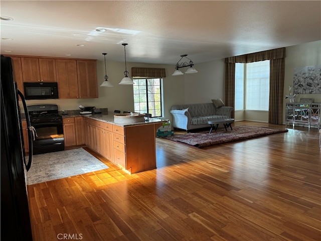 kitchen with kitchen peninsula, dark hardwood / wood-style floors, black appliances, decorative light fixtures, and light stone counters