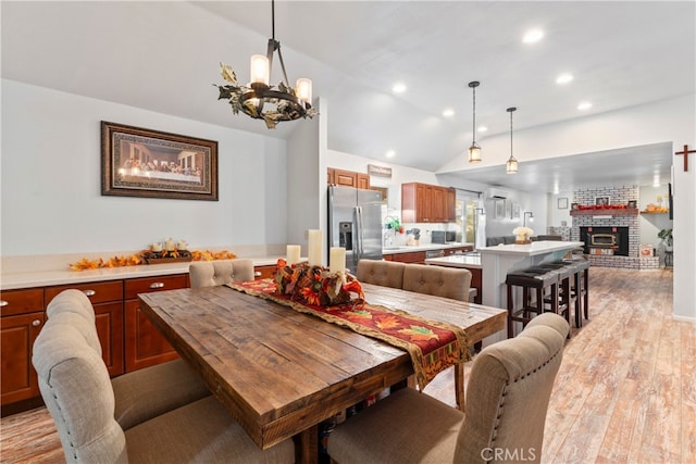 dining space with light wood-type flooring, vaulted ceiling, and a brick fireplace