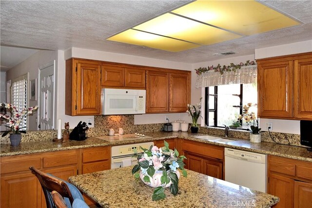 kitchen featuring sink, tasteful backsplash, light stone counters, a textured ceiling, and white appliances