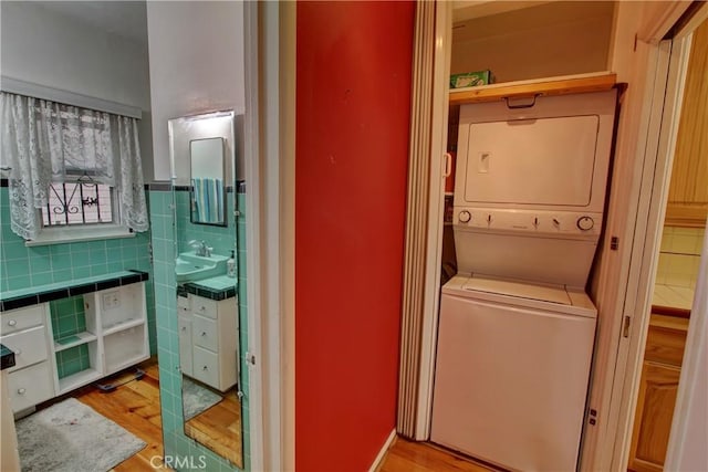 laundry room with stacked washer and dryer, sink, tile walls, and light wood-type flooring