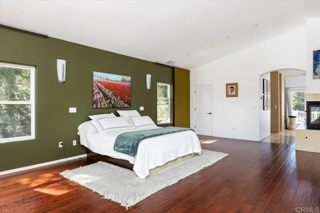 bedroom featuring a multi sided fireplace, lofted ceiling, multiple windows, and dark wood-type flooring