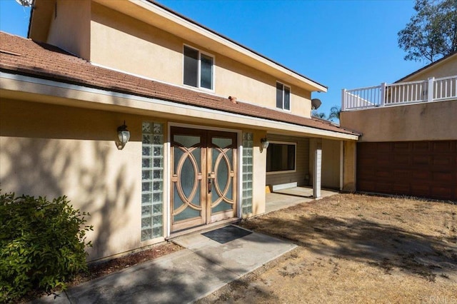 rear view of house with a balcony, a garage, and french doors