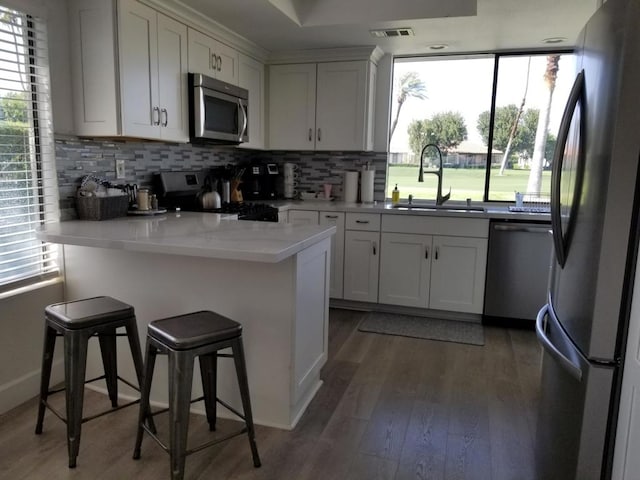 kitchen with a breakfast bar area, appliances with stainless steel finishes, white cabinetry, and a wealth of natural light