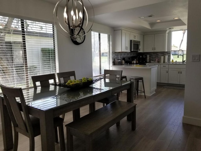 dining area featuring an inviting chandelier, a raised ceiling, sink, and dark wood-type flooring