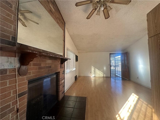 unfurnished living room featuring vaulted ceiling with beams, a brick fireplace, a textured ceiling, ceiling fan, and hardwood / wood-style floors