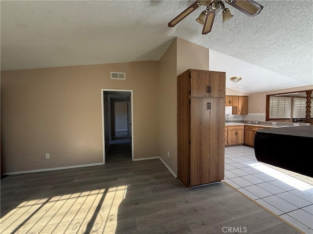 kitchen featuring vaulted ceiling, ceiling fan, a textured ceiling, and light wood-type flooring