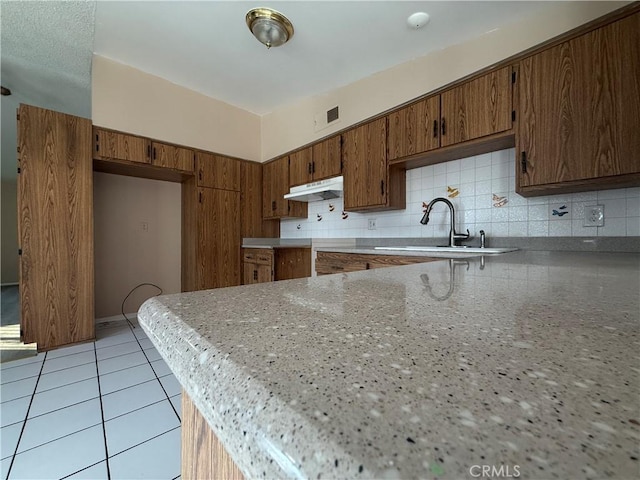 kitchen featuring kitchen peninsula, sink, decorative backsplash, and light tile patterned floors