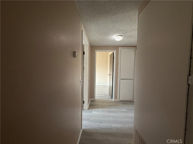 corridor with a textured ceiling and light wood-type flooring