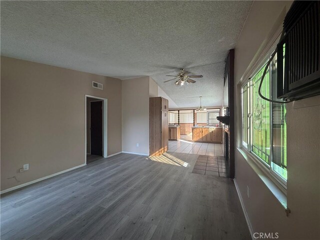 unfurnished living room featuring light hardwood / wood-style flooring, ceiling fan with notable chandelier, vaulted ceiling, and a textured ceiling