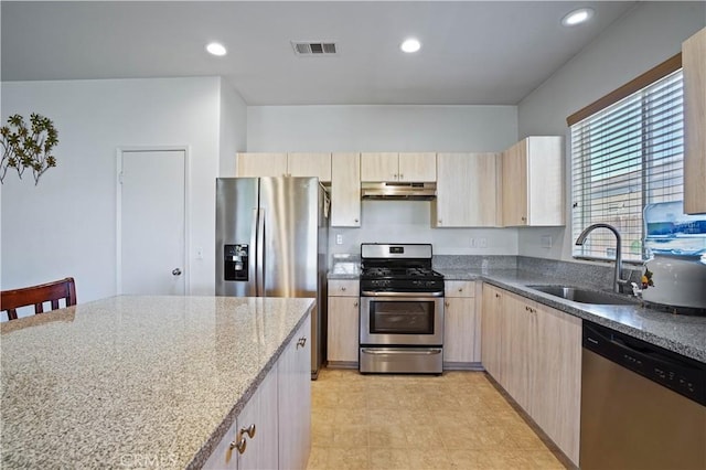 kitchen with appliances with stainless steel finishes, a kitchen breakfast bar, light brown cabinetry, light stone counters, and sink