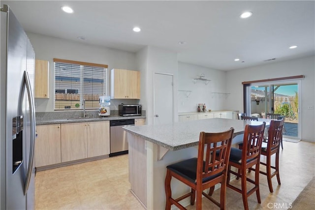 kitchen featuring sink, a center island, light stone counters, a kitchen bar, and appliances with stainless steel finishes