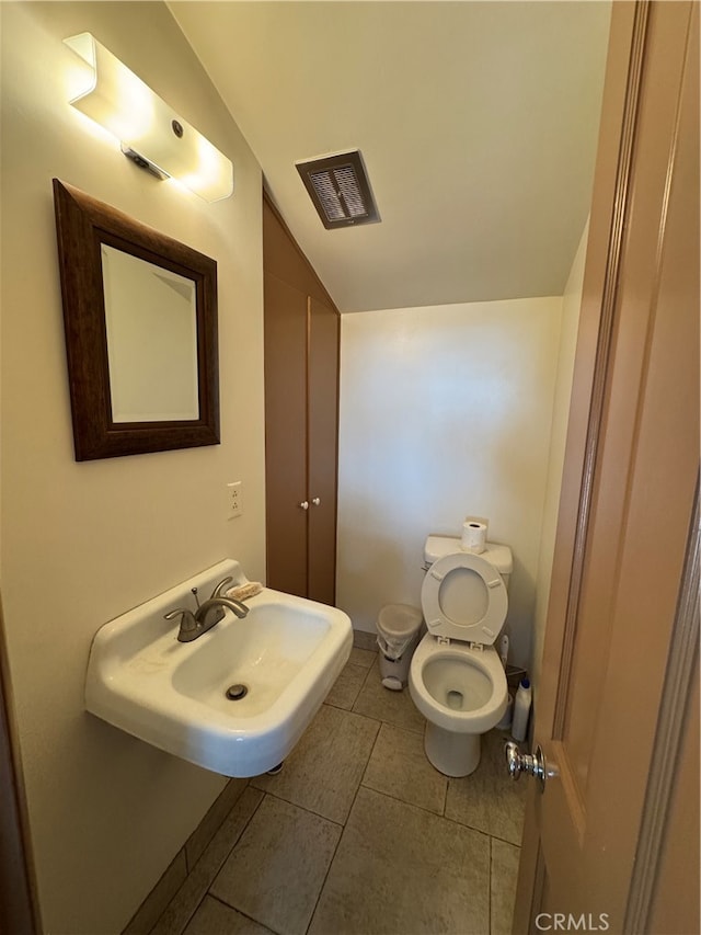 bathroom with lofted ceiling, toilet, tile patterned flooring, and sink