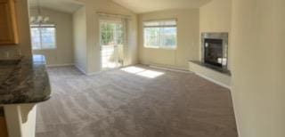 unfurnished living room with carpet flooring, a chandelier, and vaulted ceiling