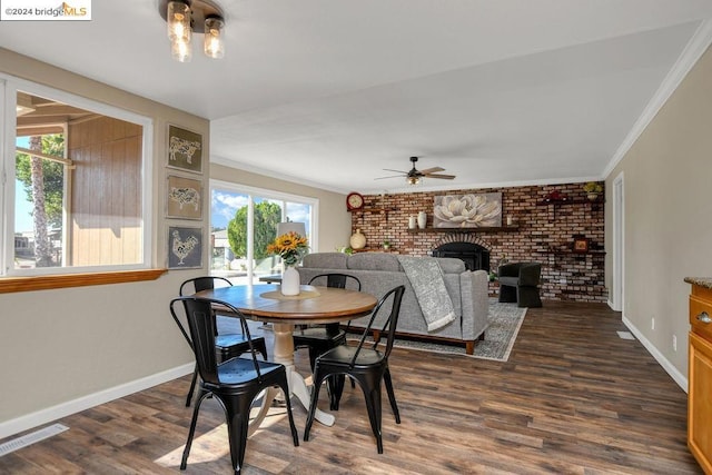 dining space with ceiling fan, a brick fireplace, brick wall, dark hardwood / wood-style floors, and crown molding