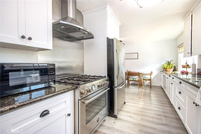 kitchen featuring light wood-type flooring, dark stone countertops, island exhaust hood, stainless steel appliances, and white cabinets