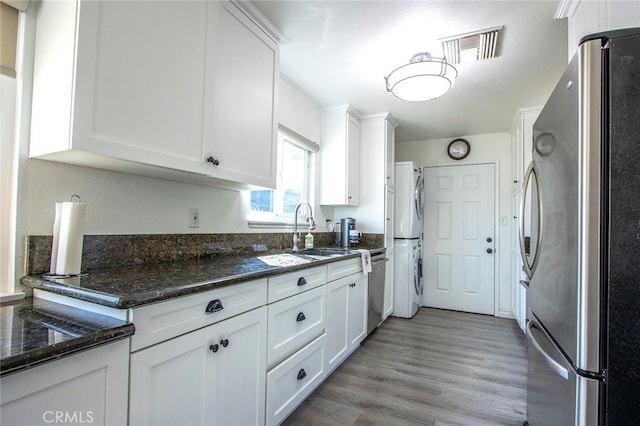 kitchen featuring sink, appliances with stainless steel finishes, dark stone countertops, white cabinets, and light wood-type flooring