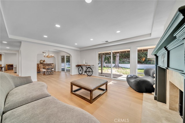 living room with a chandelier, light hardwood / wood-style floors, and a tray ceiling