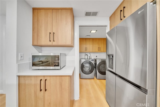 washroom with light hardwood / wood-style floors, washing machine and clothes dryer, and cabinets