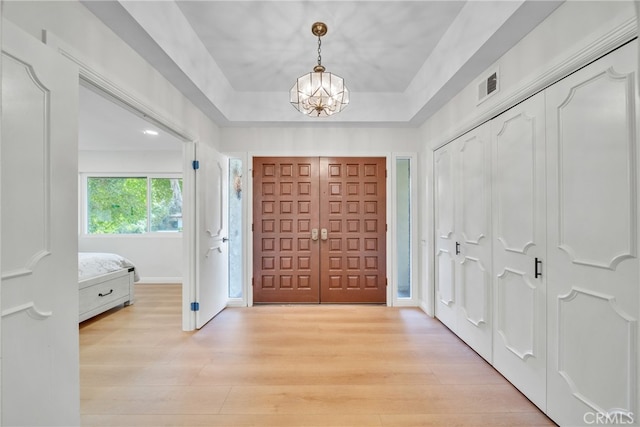 foyer entrance featuring a raised ceiling, a chandelier, and light hardwood / wood-style floors