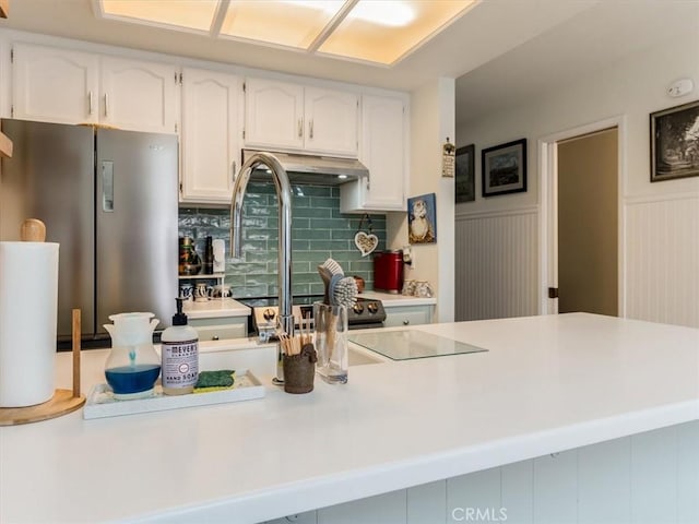 kitchen with freestanding refrigerator, a wainscoted wall, white cabinets, and under cabinet range hood