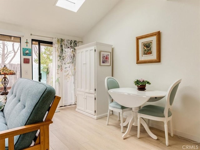 dining space with light wood finished floors, vaulted ceiling with skylight, and baseboards