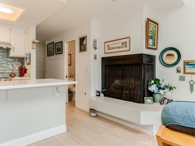 kitchen featuring a wainscoted wall, a fireplace, light wood-style flooring, and white cabinetry