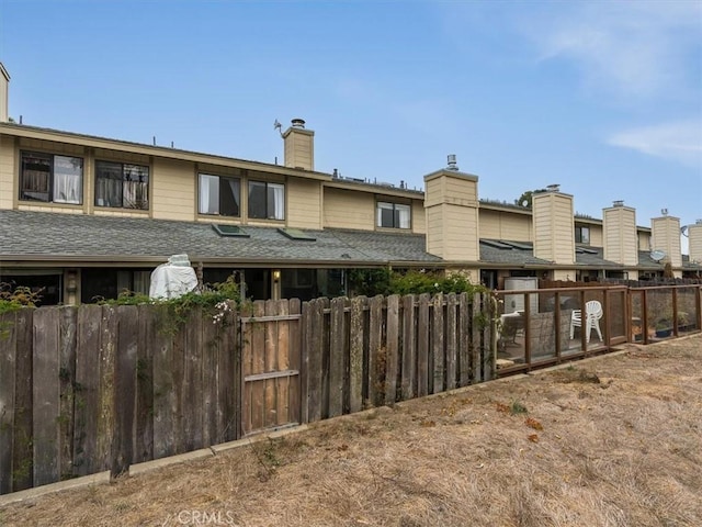 exterior space featuring roof with shingles, a chimney, and fence