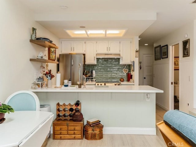 kitchen with under cabinet range hood, a peninsula, light countertops, backsplash, and freestanding refrigerator