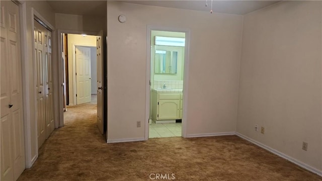 unfurnished bedroom with baseboards, connected bathroom, multiple closets, carpet, and a sink