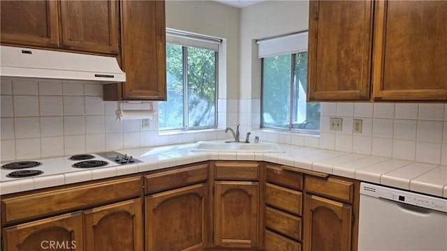 kitchen with tile counters, white appliances, backsplash, under cabinet range hood, and a sink