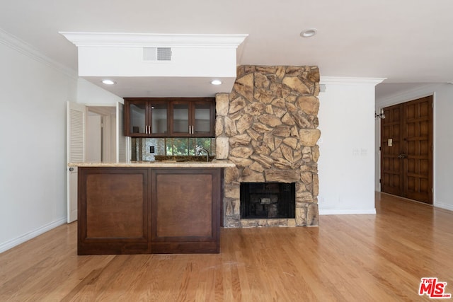 bar featuring dark brown cabinetry, crown molding, light hardwood / wood-style flooring, and a fireplace